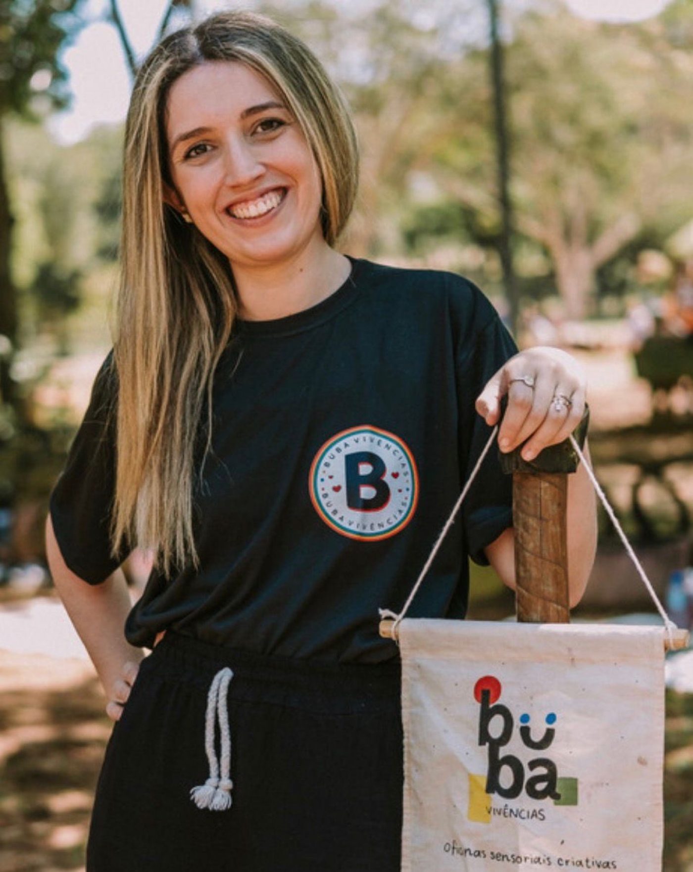 Bruna Aranda, pedagoga e idealizadora da Buba Vivências, no parque com a bandeira da marca.